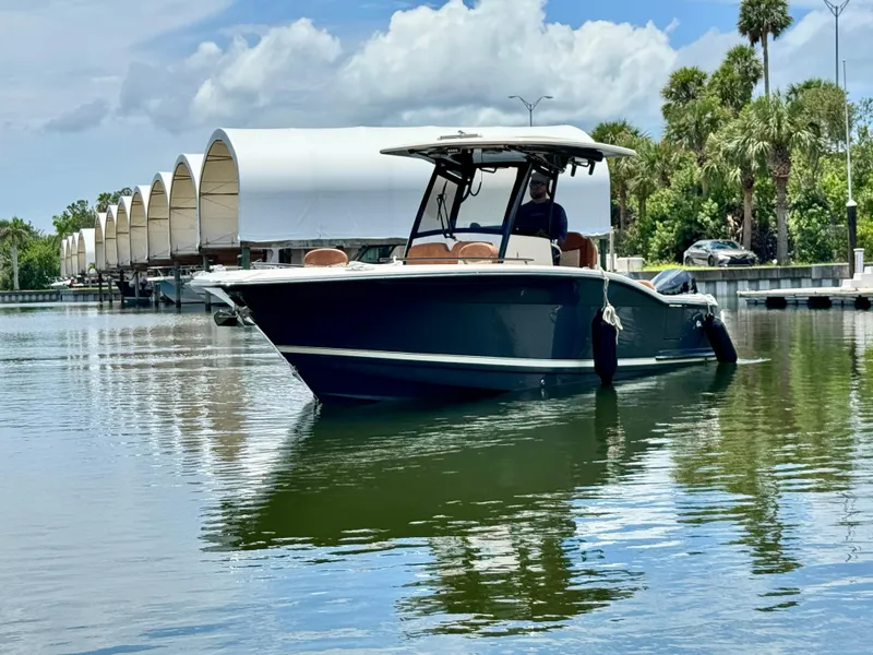 Slide: The Image of 2024 Scout 277 LXF boat on calm water near covered docks and palm trees. - 7