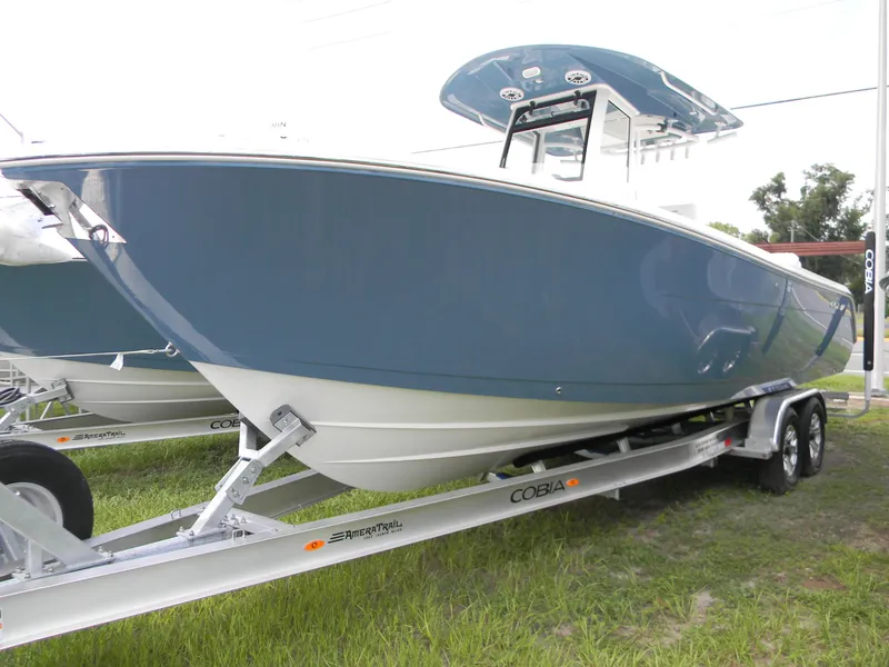The Image of 2025 Cobia 285 Center Console boat on trailer, blue hull, parked on grass. - 15