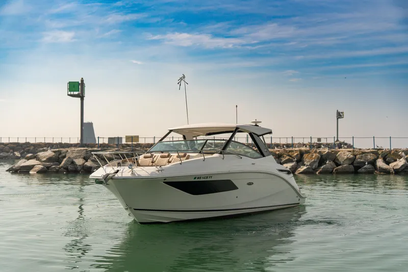 The Image of 2019 Sea Ray Sundancer 320 yacht cruising near rocky shoreline under blue sky. - 0