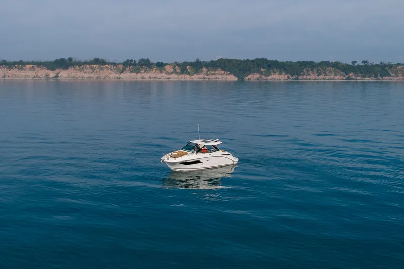 Slide: The Image of 2019 Sea Ray Sundancer 320 cruising on calm blue waters near a scenic coastline. - 19
