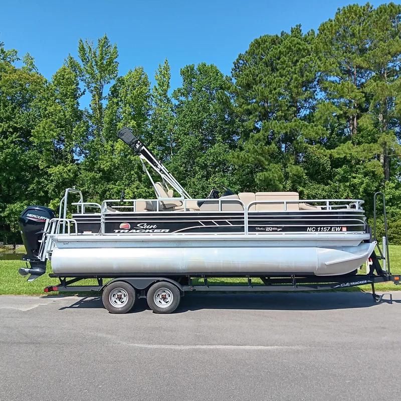The Image of 2021 Sun Tracker Fishin' Barge 20 DLX pontoon boat on trailer, parked outdoors. - 0