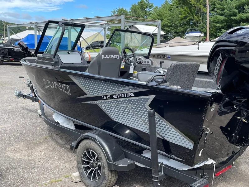 Slide: The Image of 2026 Lund 1675 Adventure Sport boat on trailer, black exterior, parked outdoors. - 11