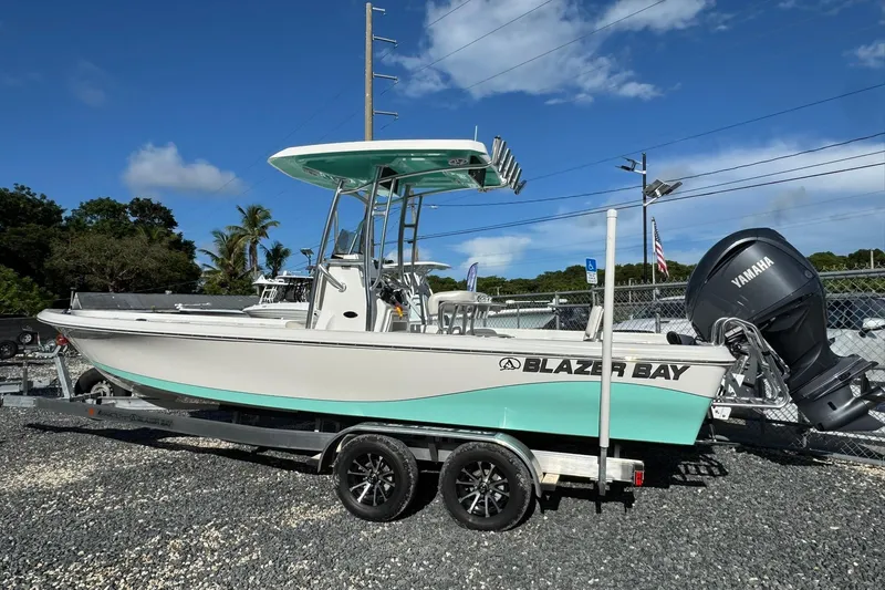 The Image of 2026 Blazer PureBay 2400 boat on trailer with Yamaha engine, parked outdoors. - 0