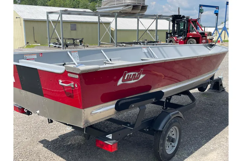 Slide: The Image of Red 2026 Lund SSV-16 boat on trailer, parked outdoors near industrial buildings. - 10