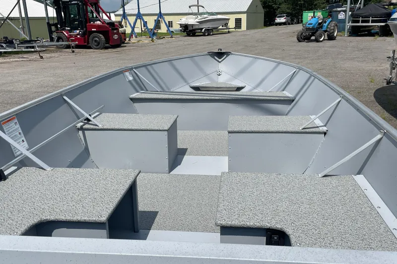 Slide: The Image of 2026 Lund SSV-16 boat interior with seating, parked outdoors near equipment and buildings. - 9