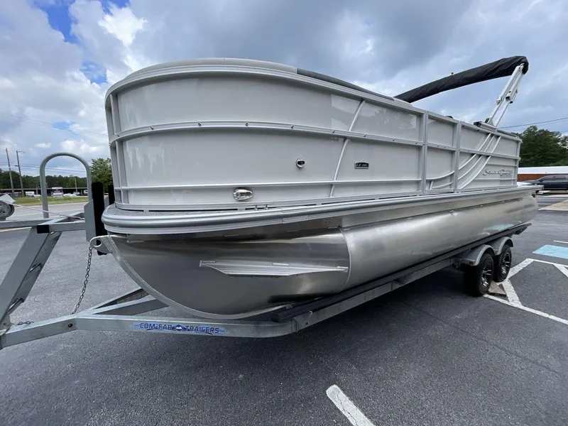 Slide: The Image of 2025 South Bay 222RSLE pontoon boat on trailer, parked outdoors under cloudy sky. - 2