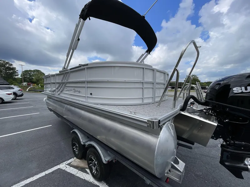 Slide: The Image of 2025 South Bay 222RSLE pontoon boat with canopy, parked on a trailer under cloudy skies. - 4