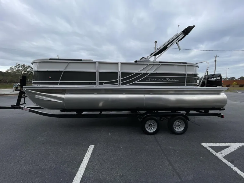 Slide: The Image of 2025 South Bay 222 RSLE pontoon boat on trailer, parked in a lot under cloudy skies. - 4