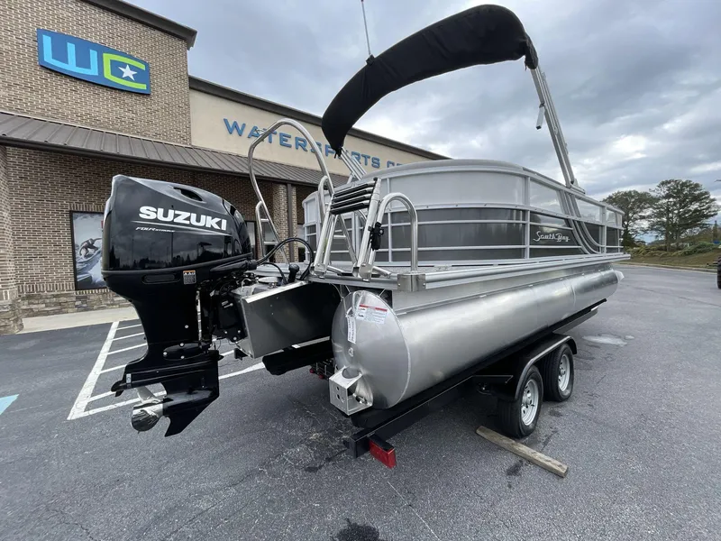 Slide: The Image of 2025 South Bay 222 RSLE pontoon boat with Suzuki engine, parked outside a water sports center. - 8