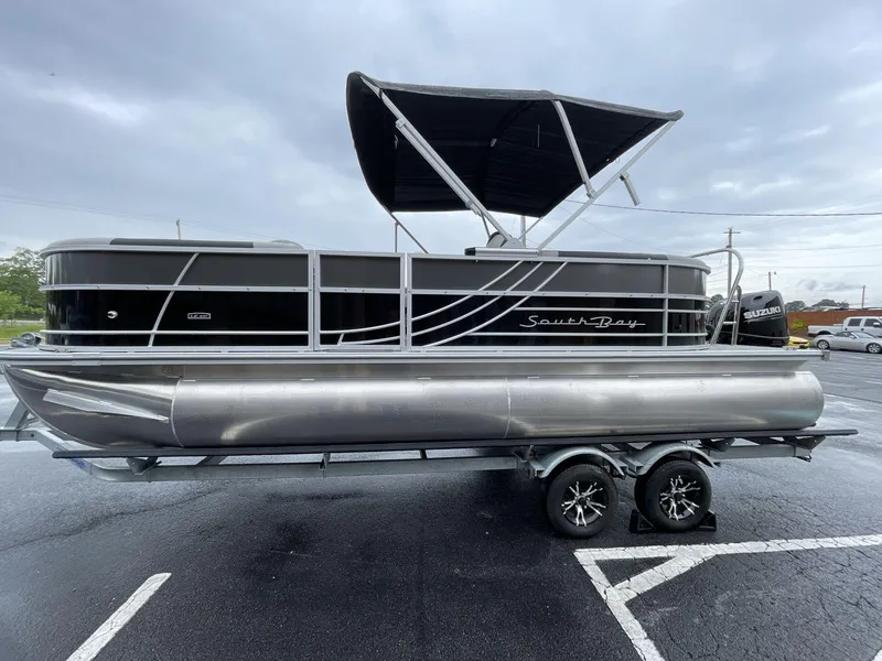 Slide: The Image of 2025 South Bay 222RSLE pontoon boat with canopy on trailer, parked outdoors. - 10