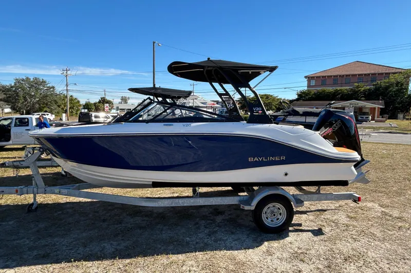 The Image of 2025 Bayliner V20 boat on trailer, blue and white design, parked outdoors. - 2