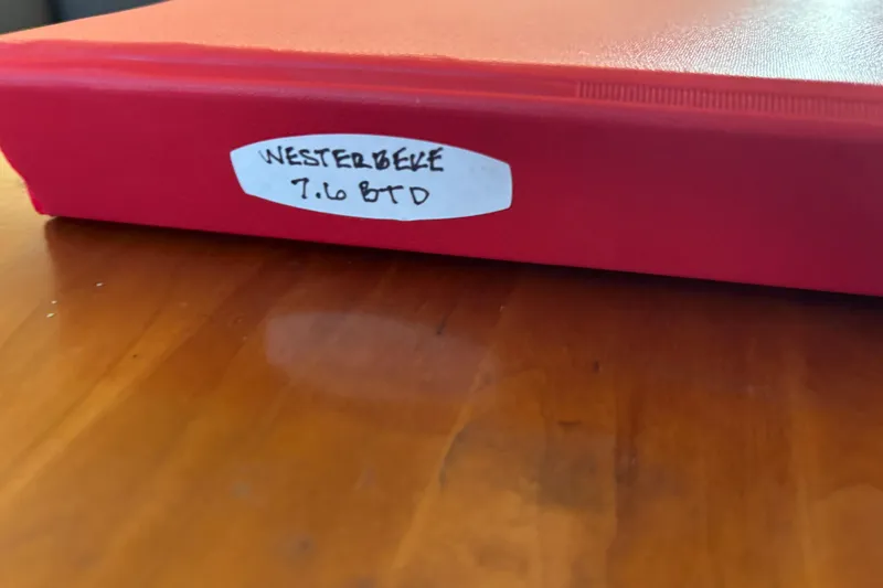 Slide: The Image of Red binder labeled "Westerbeke 7.6 BTD" on wooden surface, related to 2001 Silverton 410 Sport Bridge. - 69