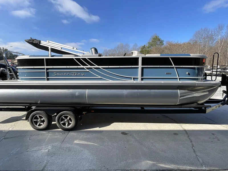 Slide: The Image of 2025 South Bay 224RSLE pontoon boat on trailer, blue and silver design, outdoors. - 7
