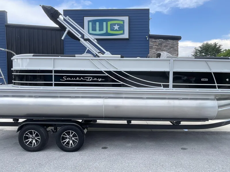 Slide: The Image of 2025 South Bay 224RSLE pontoon boat on trailer, parked outside a building. - 8
