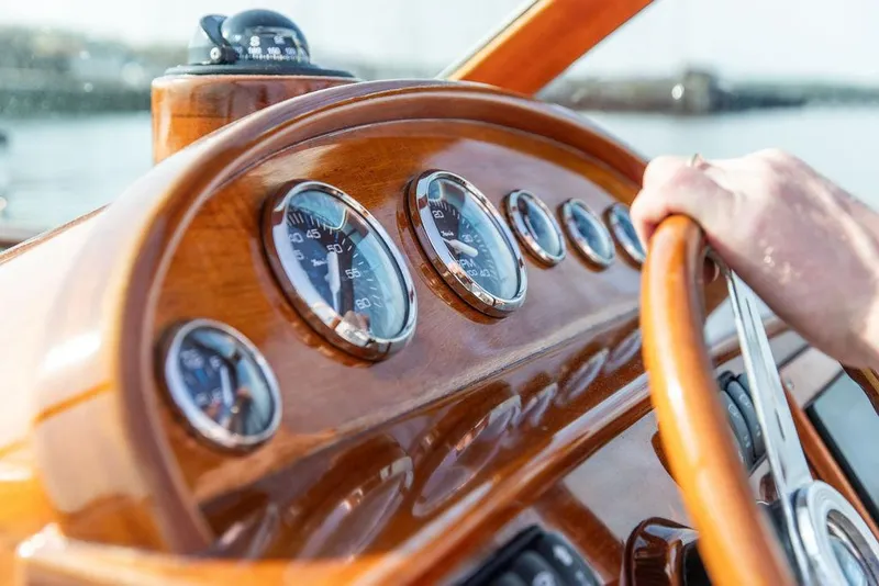 Slide: The Image of Steering wheel and dashboard of 2003 Hinckley Talaria 29R boat, featuring wooden finish and gauges. - 27