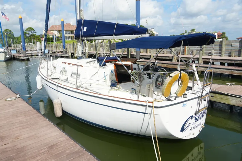 Slide: The Image of 1985 Pearson 303 sailboat docked at marina, featuring blue canopy and life preserver. - 4