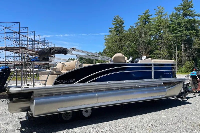 The Image of 2026 Harris Cruiser 210 pontoon boat parked outdoors on gravel, surrounded by trees. - 1