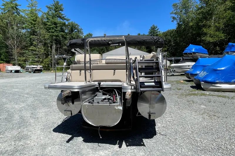 Slide: The Image of 2026 Harris Cruiser 210 pontoon boat, rear view, parked outdoors with trees and other boats. - 10