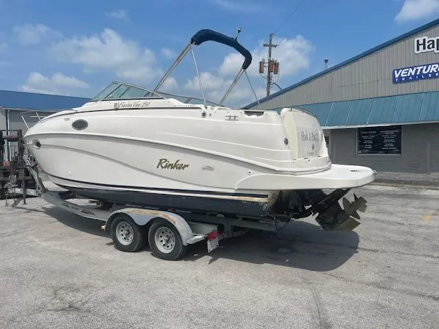 Slide: The Image of 2002 Rinker 250 FV boat on trailer, parked outside a building under a blue sky. - 2
