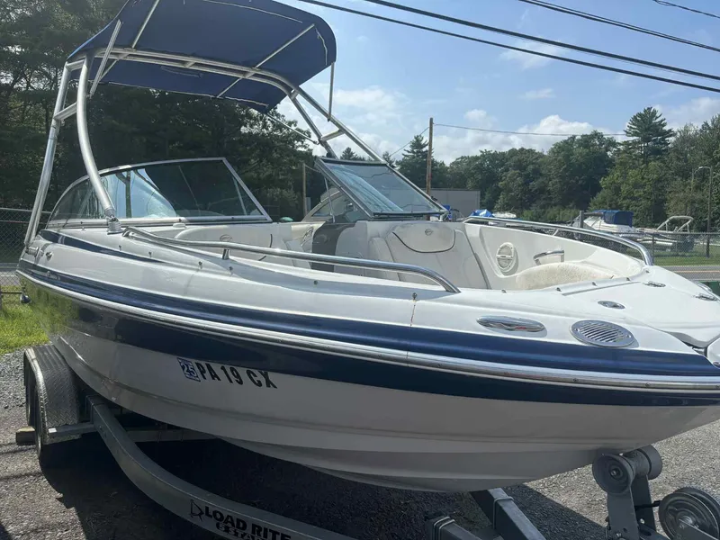 The Image of 2006 Crownline 230LS boat on trailer with blue canopy, parked outdoors. - 1