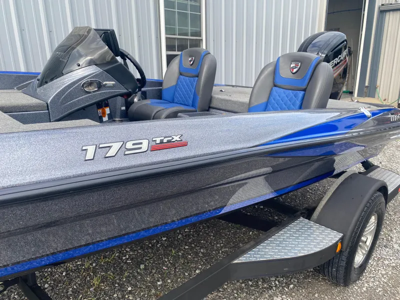 Slide: The Image of 2017 Triton 179 TrX boat with blue and gray seats, parked outside a building. - 6