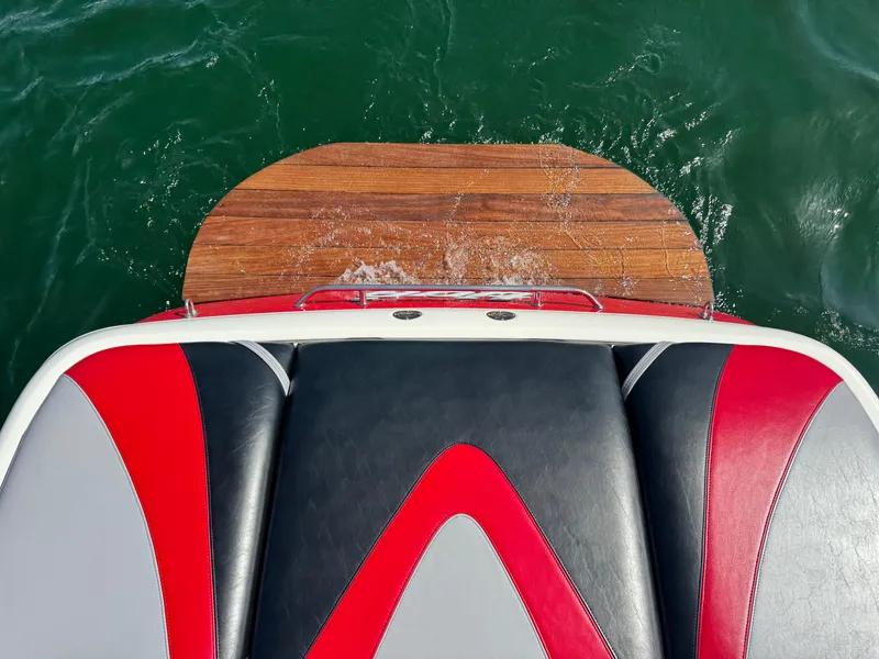 Slide: The Image of 2006 Tigé 22V boat with red and black seating, wooden swim platform, on green water. - 9