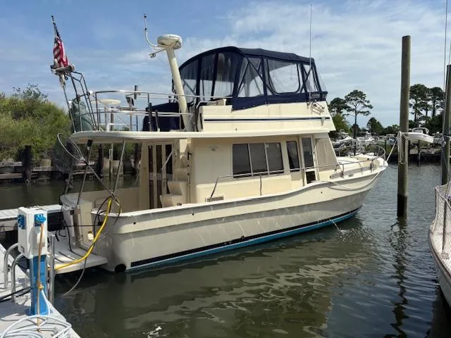 The Image of 2006 Mainship 400 Trawler docked in a marina, featuring a blue canopy and American flag. - 0