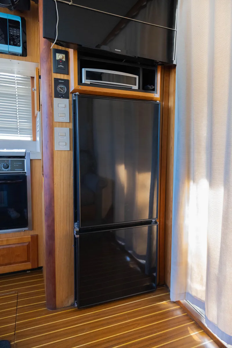 Slide: The Image of 2006 Mainship 400 Trawler interior with modern black refrigerator and wooden flooring. - 45