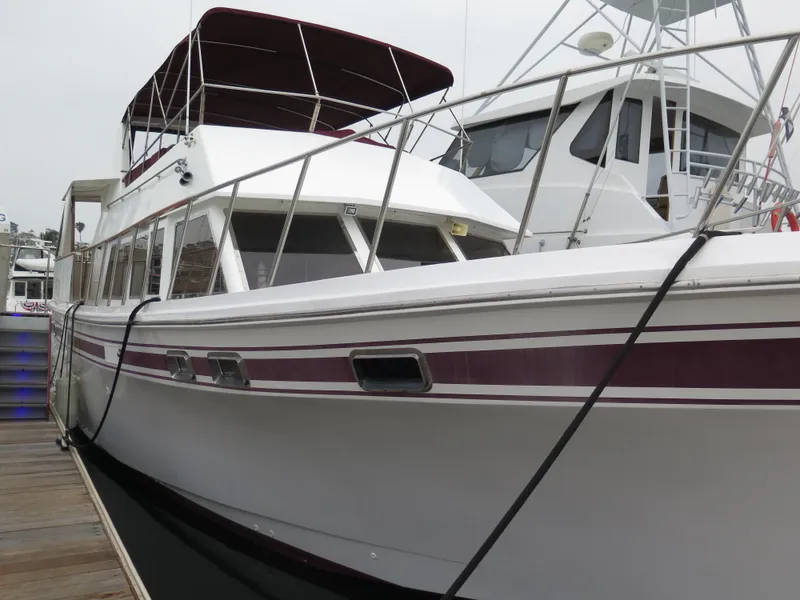 Slide: The Image of 1985 CHB Flush Deck Aftcabin yacht docked, featuring maroon accents and spacious design. - 2