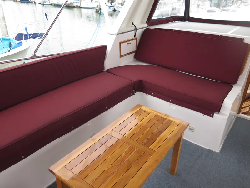 Slide: The Image of 1985 CHB Flush Deck Aftcabin with maroon seating and wooden table, docked at marina. - 8