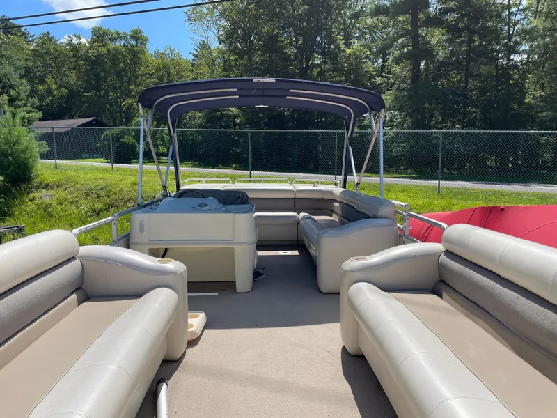 Slide: The Image of 1999 Harris Sunliner 240 pontoon boat with spacious seating and canopy, set in a lush outdoor area. - 2