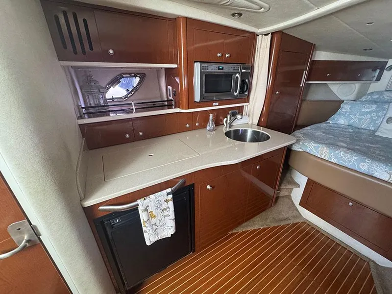 Slide: The Image of 2009 Sea Ray 330 Sundancer interior with kitchenette and bed, featuring wood cabinetry and modern appliances. - 12