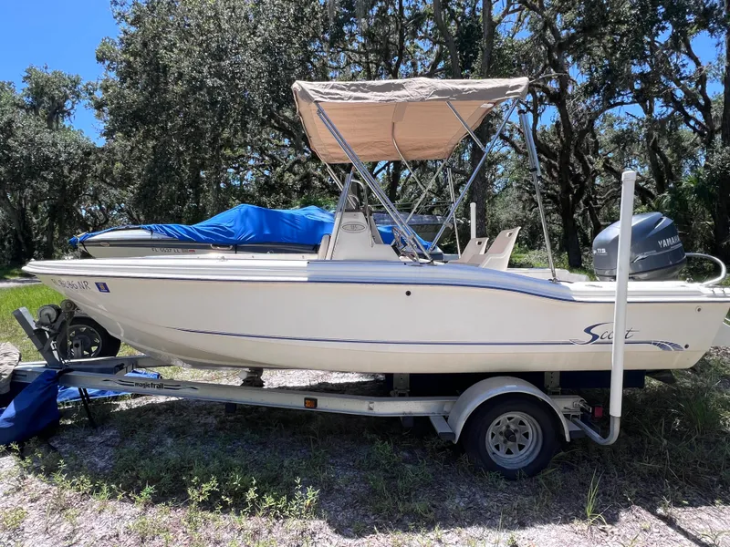 The Image of 2000 Scout 185 Sportfish boat on trailer, parked outdoors with trees in background. - 0