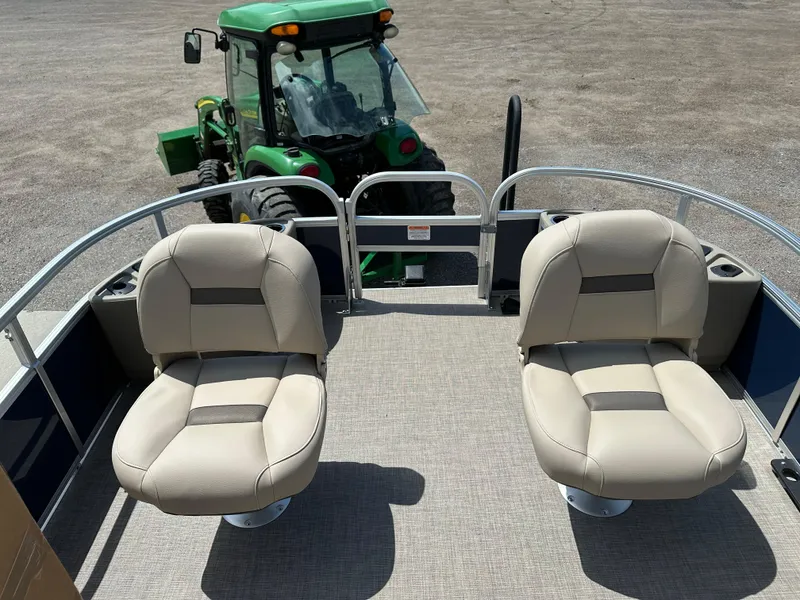 Slide: The Image of 2025 Sun Tracker Bass Buggy 18 DLX pontoon boat with beige seats, parked near a green tractor. - 12