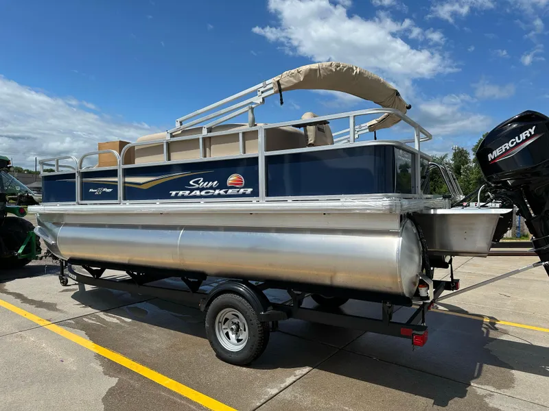 Slide: The Image of 2025 Sun Tracker Bass Buggy 18 DLX pontoon boat on trailer, under clear blue sky. - 5