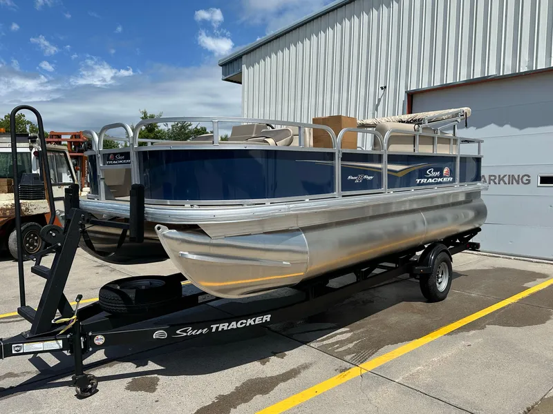 Slide: The Image of 2025 Sun Tracker Bass Buggy 18 DLX pontoon boat on trailer, parked outdoors. - 6