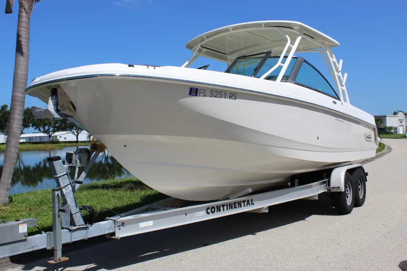 Slide: The Image of 2018 Boston Whaler 270 Vantage boat on trailer, parked near a lake. - 0