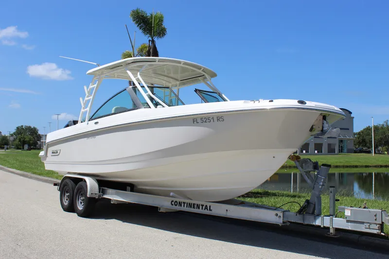 Slide: The Image of 2018 Boston Whaler 270 Vantage boat on trailer, parked near water under clear blue sky. - 14