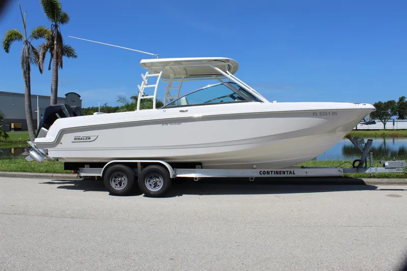 Slide: The Image of 2018 Boston Whaler 270 Vantage boat on trailer, parked near palm trees and water. - 16