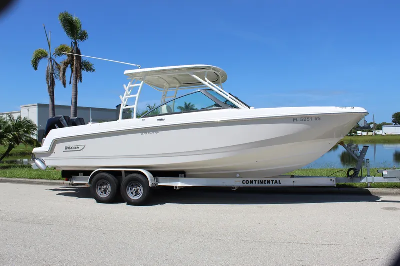 Slide: The Image of 2018 Boston Whaler 270 Vantage boat on trailer, parked near palm trees and water. - 17