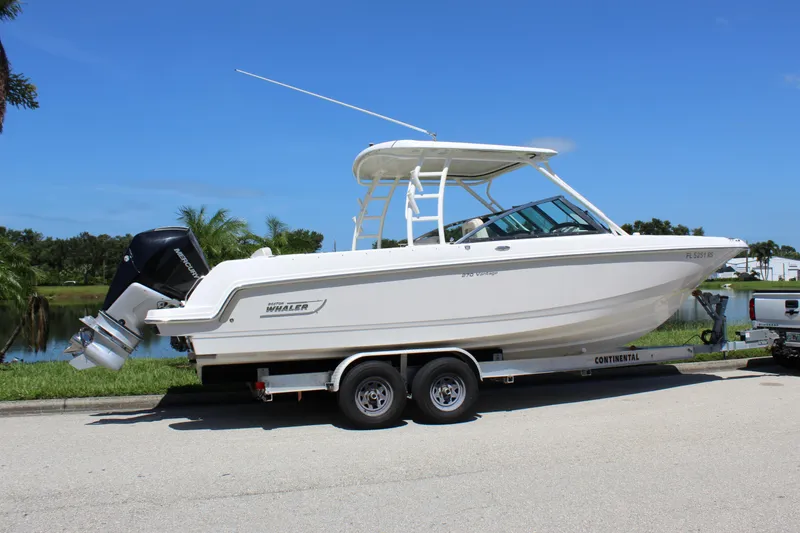 Slide: The Image of 2018 Boston Whaler 270 Vantage boat on trailer, parked near a lake under clear blue sky. - 19
