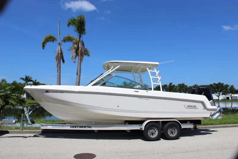 Slide: The Image of 2018 Boston Whaler 270 Vantage boat on trailer, parked near palm trees and water. - 4