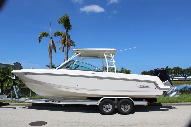 Slide: The Image of 2018 Boston Whaler 270 Vantage boat on trailer, parked near palm trees under blue sky. - 5