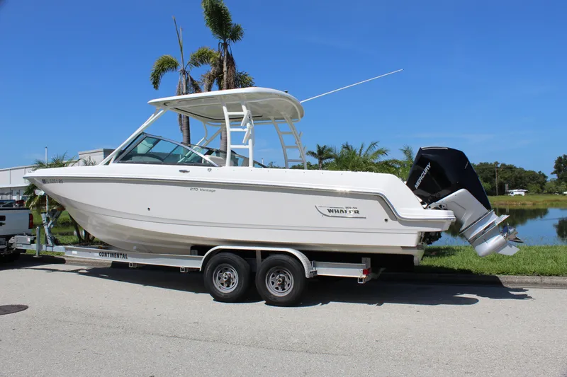 Slide: The Image of 2018 Boston Whaler 270 Vantage boat on trailer, parked near water and palm trees. - 6