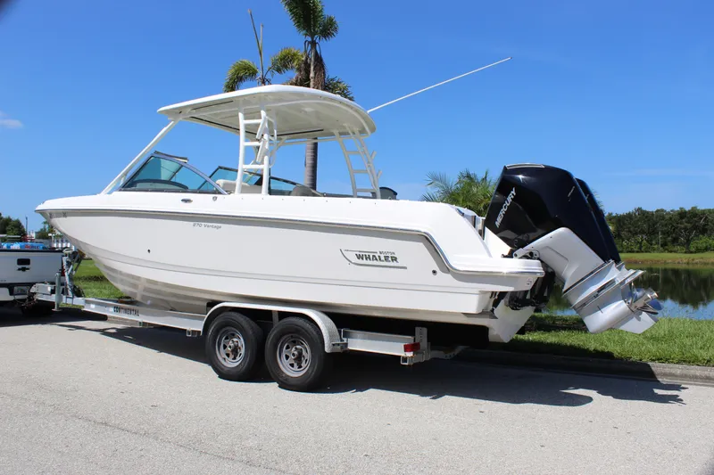 Slide: The Image of 2018 Boston Whaler 270 Vantage boat on trailer, parked near a lake under clear blue sky. - 7