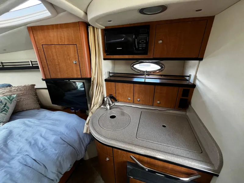 Slide: The Image of 2006 Sea Ray 290 Sundancer interior with kitchenette and bed, featuring wood cabinetry and modern amenities. - 16