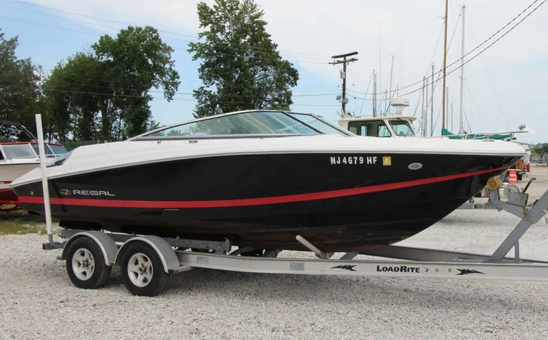 The Image of 2009 Regal 2200 Bowrider boat on trailer, black with red stripe, parked outdoors. - 0