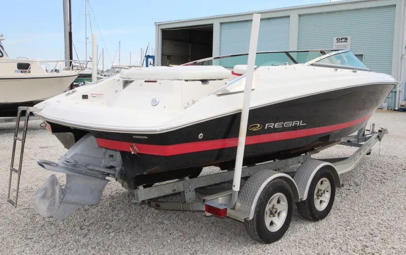 Slide: The Image of 2009 Regal 2200 Bowrider boat on trailer, parked outdoors near a marine facility. - 4