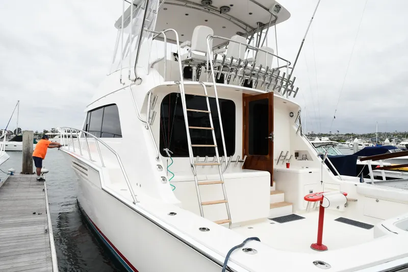 Slide: The Image of 1988 Bertram 54 Convertible yacht docked at marina, with person cleaning the side. - 1