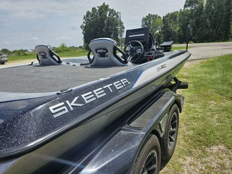 Slide: The Image of 2025 Skeeter FXR21 PRO boat on trailer, parked on grass, sunny day. - 13